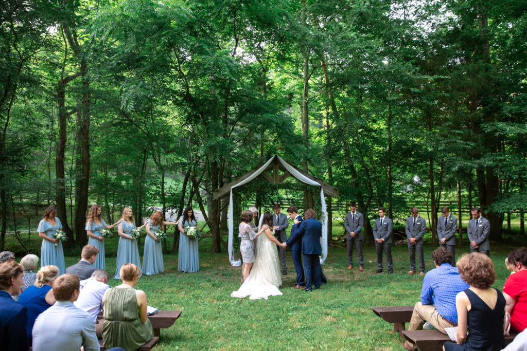 Prayer ceremony with bride and groom under a wooded arbor in Tennessee Outdoor Farm Wedding